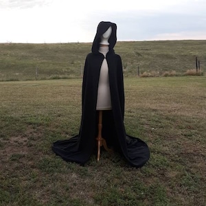May include: A black hooded cape with a long train, displayed on a mannequin against a grassy background.