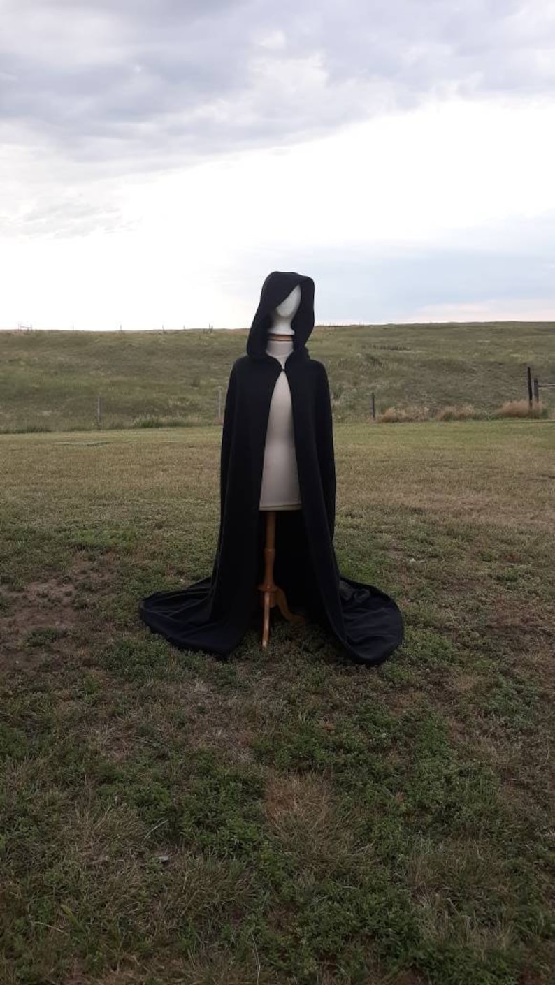May include: A black hooded cape with a long train, displayed on a mannequin against a grassy background.