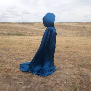 May include: A long, flowing blue satin cape with a large hood. The cape is draped over a field of dry grass.