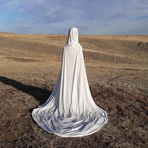 May include: A white hooded cape with a long train, photographed in a field.