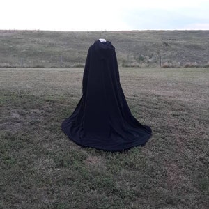 May include: A black cape with a hood, lying on a grassy field.