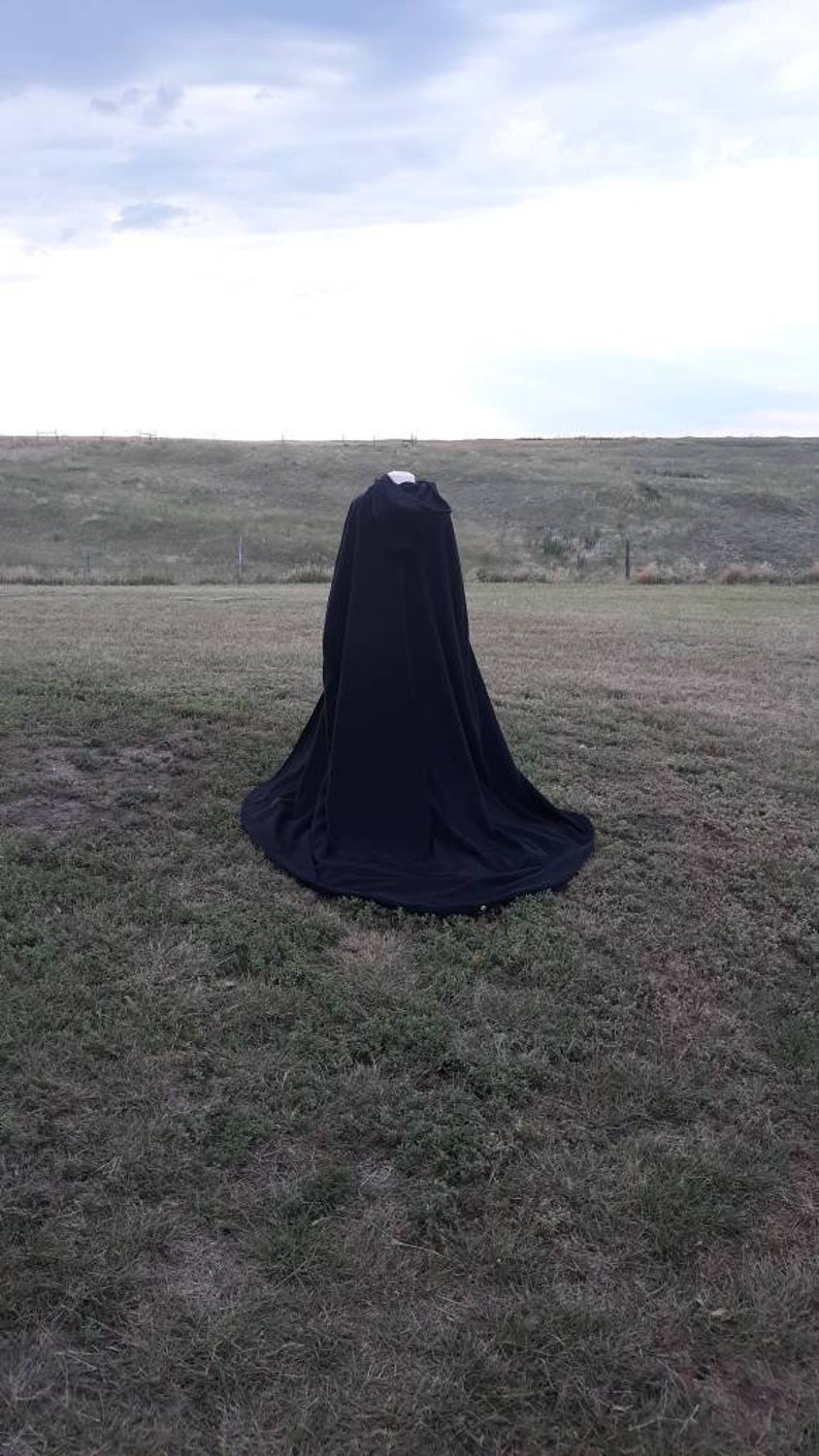 May include: A black cape with a hood, lying on a grassy field.