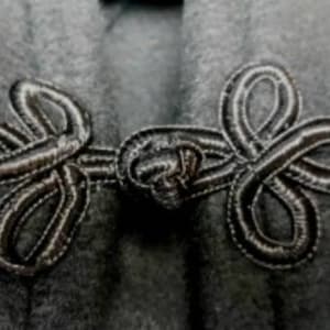 May include: A close-up of a black fabric with a decorative knotted closure. The closure is made of two loops that are intertwined and secured with a knot.