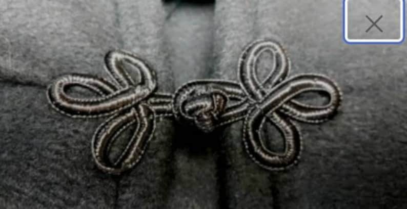 May include: A close-up of a black fabric with a decorative knotted closure. The closure is made of two loops that are intertwined and secured with a knot.