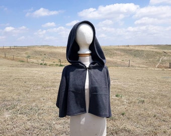 May include: A dark gray hooded cape with a simple design. The cape is made of a soft, comfortable fabric and has a tie closure at the neck.