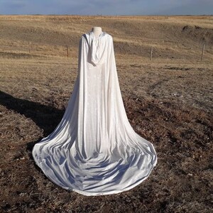 May include: A white hooded cape with a long train, laying on a field of dry grass.