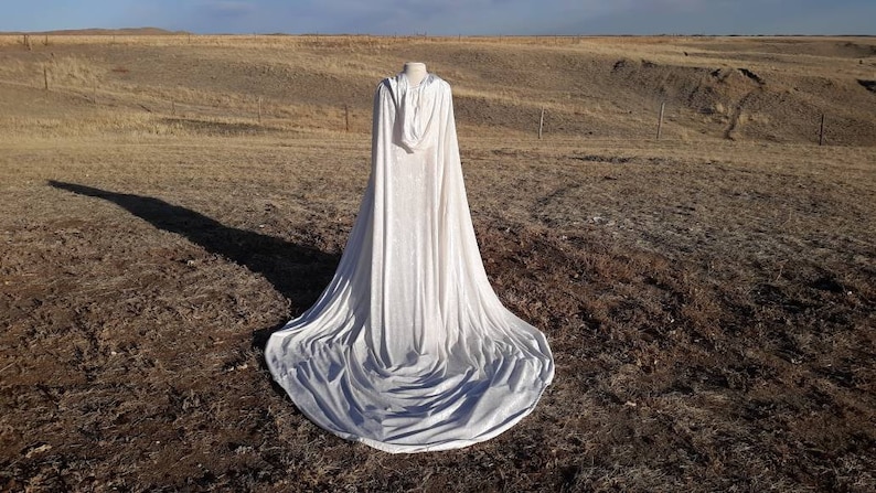 May include: A white hooded cape with a long train, laying on a field of dry grass.