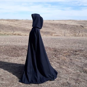 K&ouml;nnte beinhalten: Ein schwarzer Kapuzenumhang mit langem, flie&szlig;endem Design. Der Umhang ist aus einem weichen, bequemen Stoff gefertigt und perfekt, um jedem Outfit einen Hauch von Geheimnis und Intrige zu verleihen.