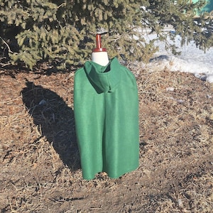 May include: A green hooded cape with a long, flowing design. The cape is made of a soft, plush fabric and has a simple, elegant style.