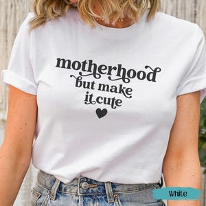 Könnte beinhalten: Weißes T-Shirt mit dem Text "motherhood but make it cute" in schwarzer Schrift und einem schwarzen Herz-Grafik. Das Shirt hat kurze Ärmel und einen Rundhalsausschnitt.