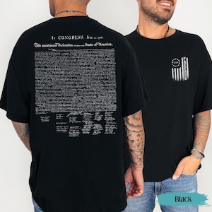 May include: Black t-shirt featuring the text "In Congress, July 4, 1776. The unanimous Declaration of the States of America" on the back. The front displays a flag design with the word "FREEDOM".