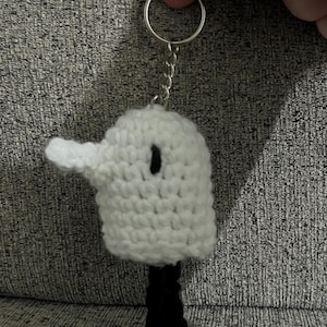 May include: White crocheted bird keychain with black legs and a black eye. The keychain is attached to a silver key ring.