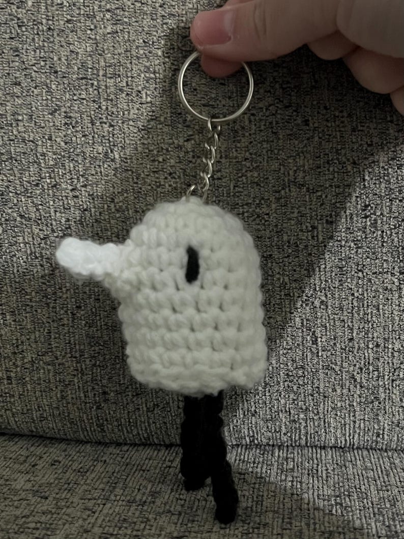 May include: White crocheted bird keychain with black legs and a black eye. The keychain is attached to a silver key ring.