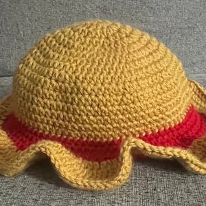 May include: A crocheted hat with a yellow crown and a red brim. The brim has a ruffled edge.