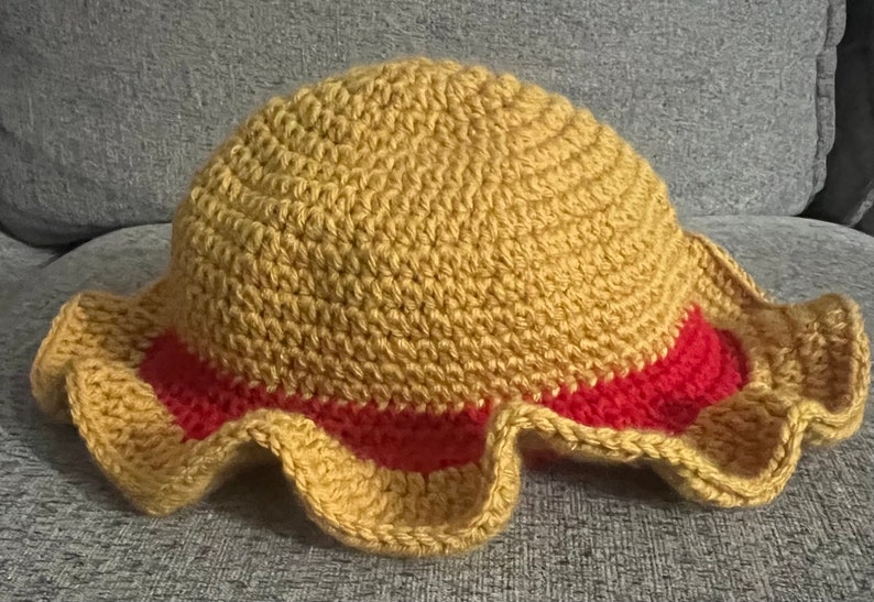 May include: A crocheted hat with a yellow crown and a red brim. The brim has a ruffled edge.