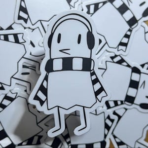 May include: A white sticker of a cartoon ghost wearing headphones and a black and white striped scarf. The ghost has a small mouth and large eyes.