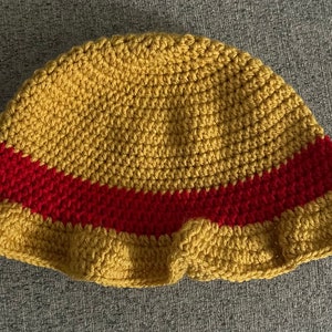 May include: A crocheted bucket hat with a yellow crown and a red band around the brim.