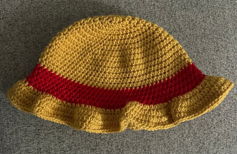May include: A crocheted bucket hat with a yellow crown and a red band around the brim.