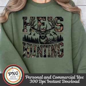 May include: Green sweatshirt with a camouflage print design featuring the text "He's Hunting" and a deer silhouette.