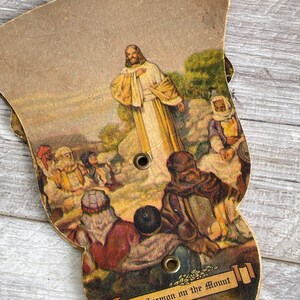 May include: A vintage paper fan with a colorful illustration of Jesus delivering the Sermon on the Mount. The fan is decorated with a gold ribbon with the text "The Sermon on the Mount".