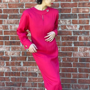 May include: A bright pink dress with long sleeves and a keyhole neckline. The dress has a fitted silhouette and a slightly flared skirt. The dress is made of a smooth, lightweight fabric.