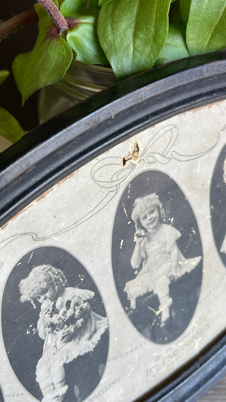 May include: A vintage oval picture frame with a black wooden frame and a white mat. The frame contains three black and white photos of young girls. The photos are oval shaped and have a decorative border. The text "The Three Sisters" is printed on the bottom of the frame.