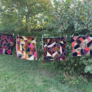 May include: Four square fabric pieces featuring a patchwork of multi-colored velvet and textile scraps joined with dark zigzag stitching. The pieces are hung side-by-side on a green clothesline, displaying various geometric shapes and textures.