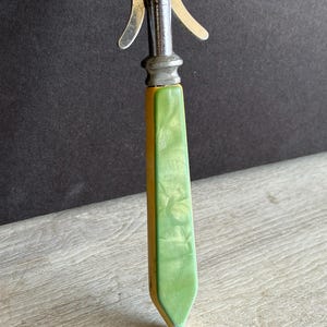 May include: A silver and green kitchen utensil with a long handle. The handle is made of green plastic with a yellow stripe. The utensil is labeled "Stainless Chrome Plated".