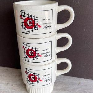 May include: Three stacked white ceramic mugs. Each mug features a red circle with a white "C" inside, a black grid, and the text "CENTRAL INSURANCE Agency". The mugs have a handle and a ribbed base.