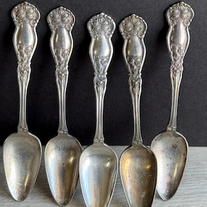 May include: Set of five silver spoons with ornate floral designs on the handles. The spoons have a teardrop-shaped bowl.