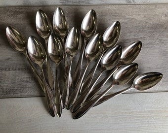 May include: A group of 12 silver spoons arranged in a fan shape. The spoons are all the same size and shape, and they have a shiny, polished finish.