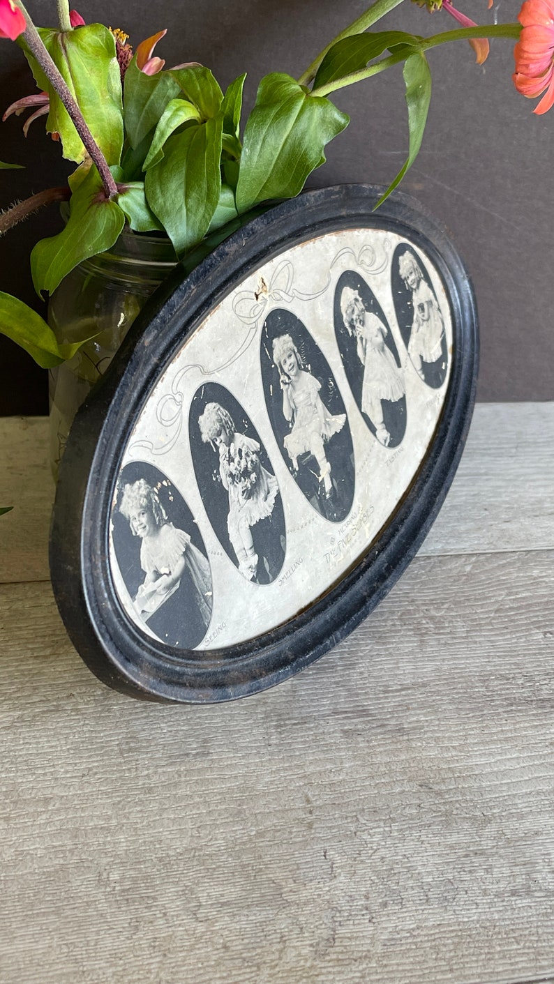 May include: A black oval frame with a white background and six black and white photos of children. The photos are arranged in a circle and each photo has a name written below it. The text "The Time Swings" is written in a circle around the photos.