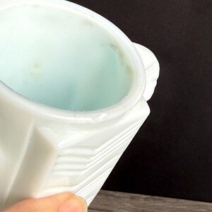 May include: A white, geometric-patterned container with a light blue interior. The container has a handle and a slightly textured surface. The image is a close-up shot, highlighting the details of the object.