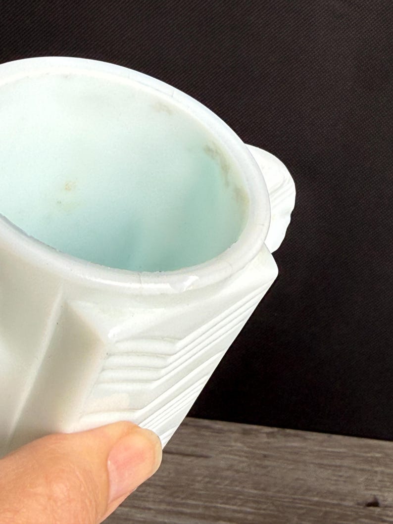 May include: A white, geometric-patterned container with a light blue interior. The container has a handle and a slightly textured surface. The image is a close-up shot, highlighting the details of the object.