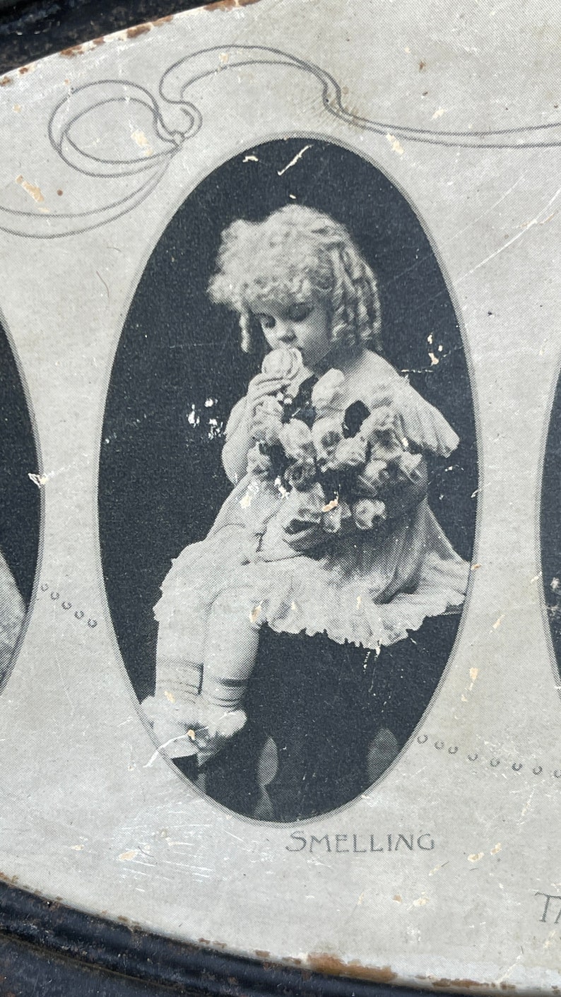 May include: Black and white photo of a young girl in a white dress holding a bouquet of flowers. The photo is in an oval frame with the word "SMELLING" printed below it.