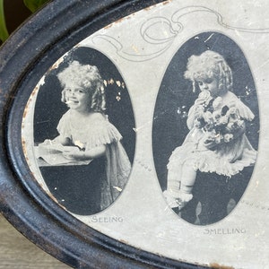 May include: A vintage oval tin with a black painted exterior and a white interior. The tin features three black and white images of children, each with a different caption: "Seeing", "Smelling", and "Tasting".