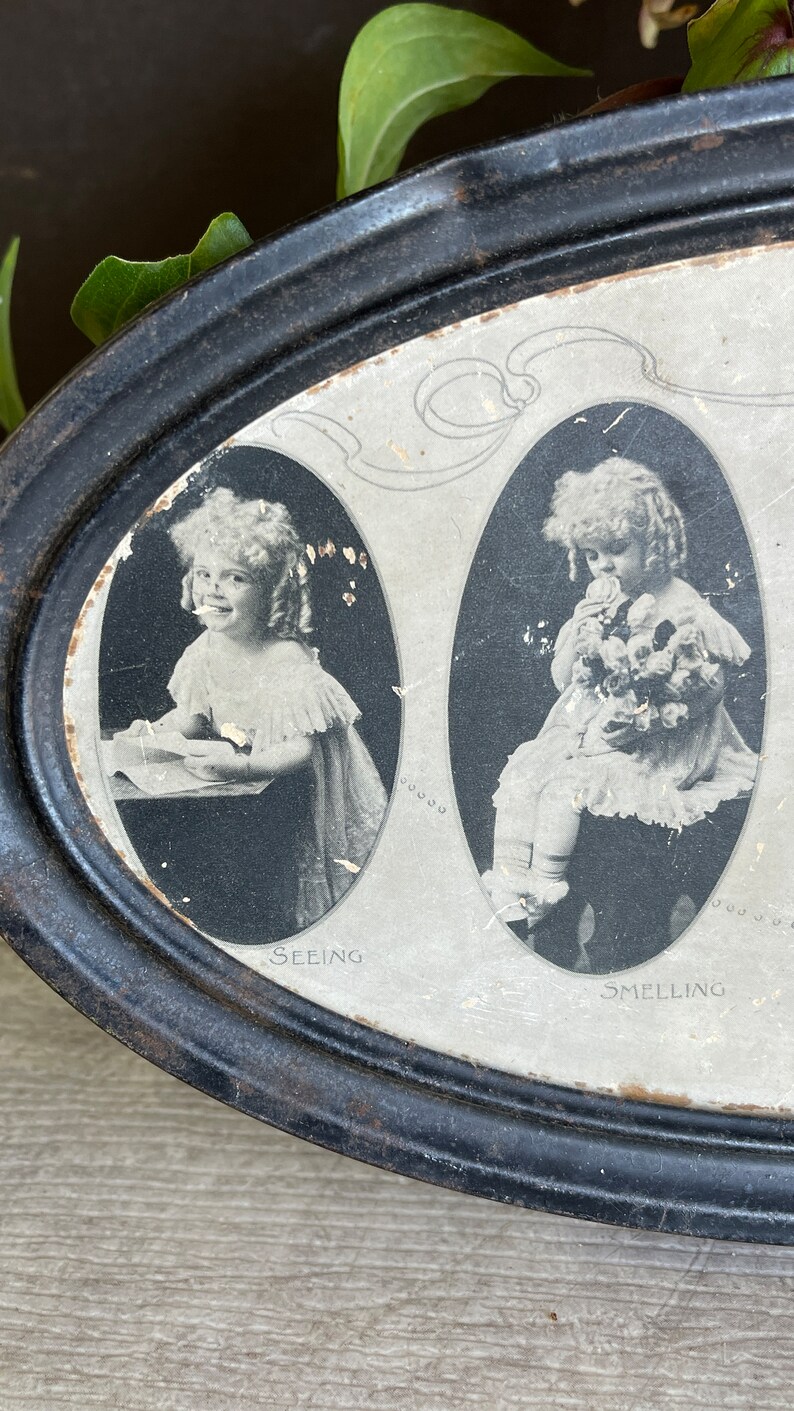 May include: A vintage oval tin with a black painted exterior and a white interior. The tin features three black and white images of children, each with a different caption: "Seeing", "Smelling", and "Tasting".