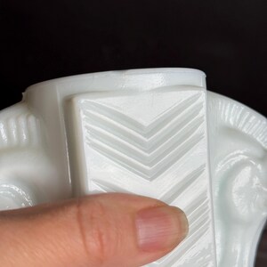 May include: A close-up of a white, Art Deco-style horse head figurine. The figurine features a geometric design with chevron patterns. The horse's head is visible, with details of the eye and mane. The figurine is made of a glossy, opaque material.