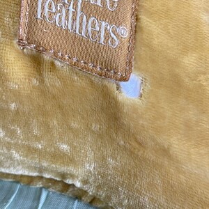K&ouml;nnte beinhalten: Ein senfgelbes Samtkissen mit hellblauem Besatz und einem braunen Etikett mit der Aufschrift "square feathers".