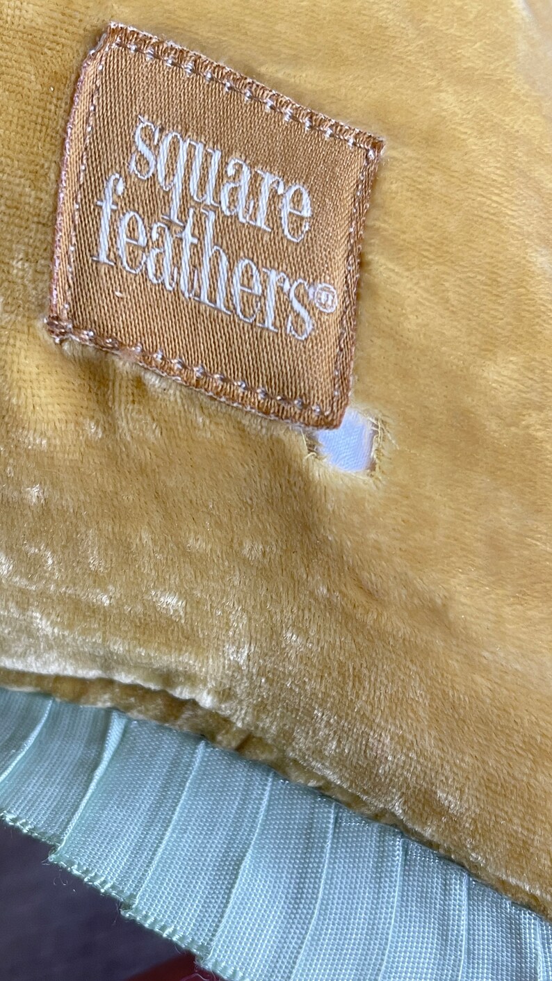 K&ouml;nnte beinhalten: Ein senfgelbes Samtkissen mit hellblauem Besatz und einem braunen Etikett mit der Aufschrift "square feathers".