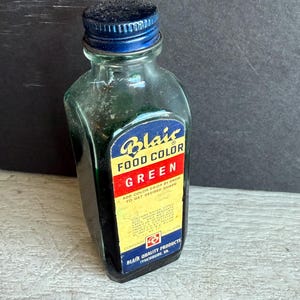 May include: A vintage glass bottle of Blair Food Color Green. The label features the brand name and product information. The bottle has a blue cap and is filled with green liquid. The text on the label reads "Add color drop by drop to get desired shade."