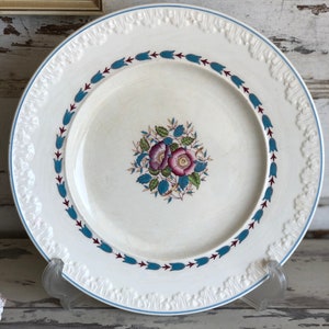 May include: White ceramic dinner plate with a blue and red floral design. The plate has a raised rim with a decorative pattern.