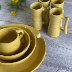 May include: A set of four yellow ceramic mugs with handles, and three yellow ceramic bowls stacked on top of each other. The mugs and bowls are all the same shade of yellow.