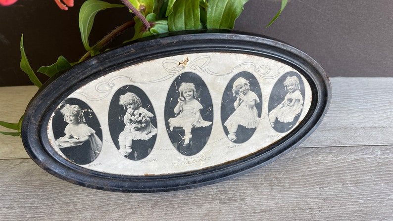May include: An oval-shaped black framed picture with a white background featuring five black and white photos of young girls in various poses. The photos are arranged in a row and each has a title below it. The title below the first photo is "Smiling", the second is "Holding", the third is "The Five Bunnies", the fourth is "Tattling", and the fifth is "Crying".
