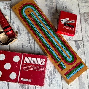 May include: A collection of vintage board games, including a cribbage board, a deck of "Lord Baltimore Pinochle" playing cards, a box of dominoes, and a box of cribbage pegs.