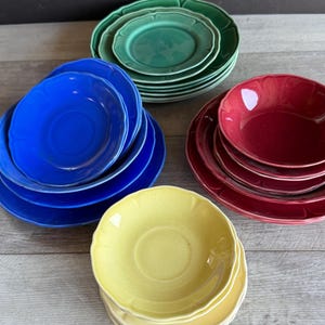 May include: Set of four stacks of vintage ceramic plates in blue, green, yellow, and red. Each stack has a different color and features a scalloped edge.
