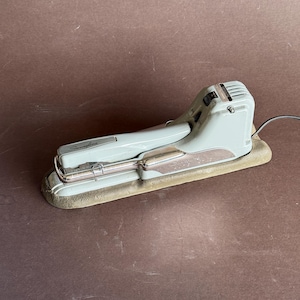 May include: A vintage light blue Swingline electric stapler with a black cord. The stapler has a metal base and a silver handle.