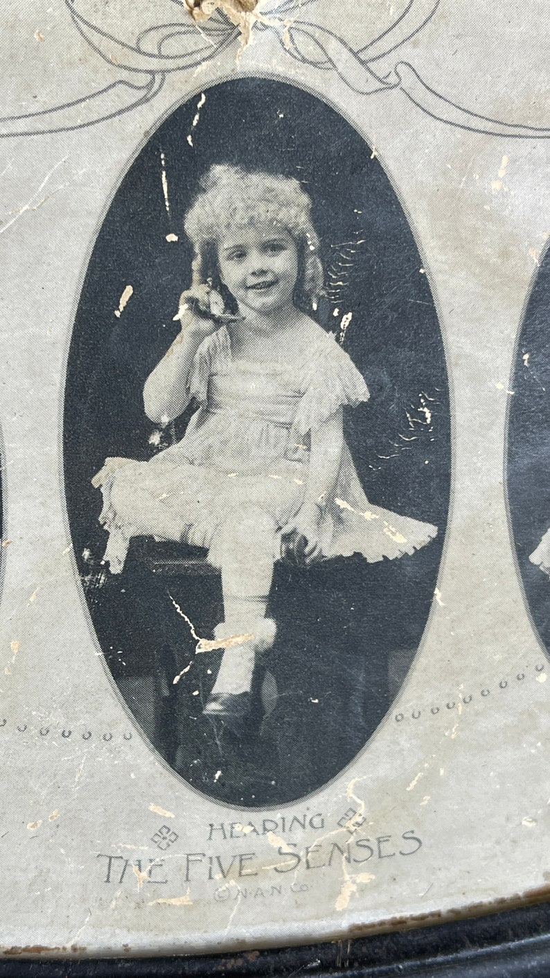 May include: Black and white photo of a young girl in a white dress holding a toy telephone. The photo is framed in an oval and is part of a larger image depicting the five senses. The text "Hearing" and "The Five Senses" is visible below the photo.