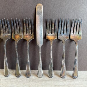 May include: Set of eight vintage silver-plated forks and a butter knife. The forks have ornate handles and tines. The knife has a rounded blade and a similar handle to the forks.
