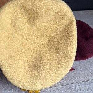 Puede incluir: Primer plano de dos boinas. La boina delantera es de color amarillo claro, mientras que la segunda es de color burdeos oscuro. Los sombreros est&aacute;n hechos de un material suave similar al fieltro, ideal para oto&ntilde;o o invierno.